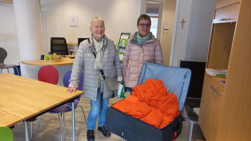Zwei Frauen hinter einem Koffer, der voll mit orangenfarbenen Schals ist
