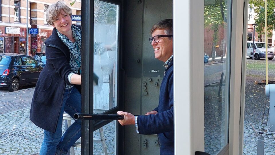 Hier sieht man zwei Menschen die eine Telefonzelle putzen.